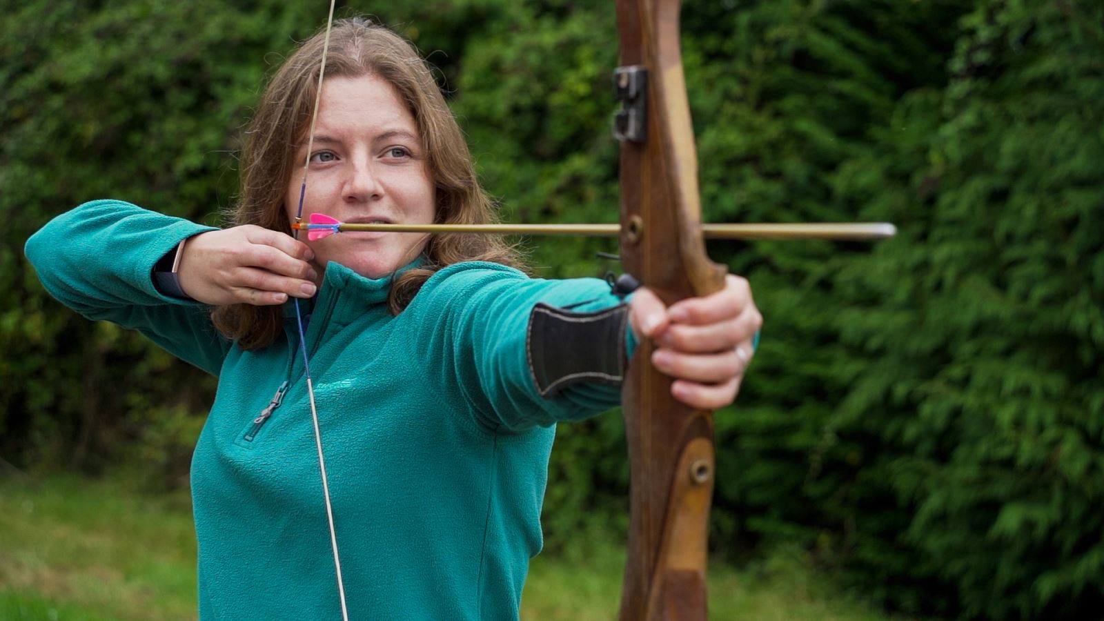 A woman draws back the bow as she learns archery